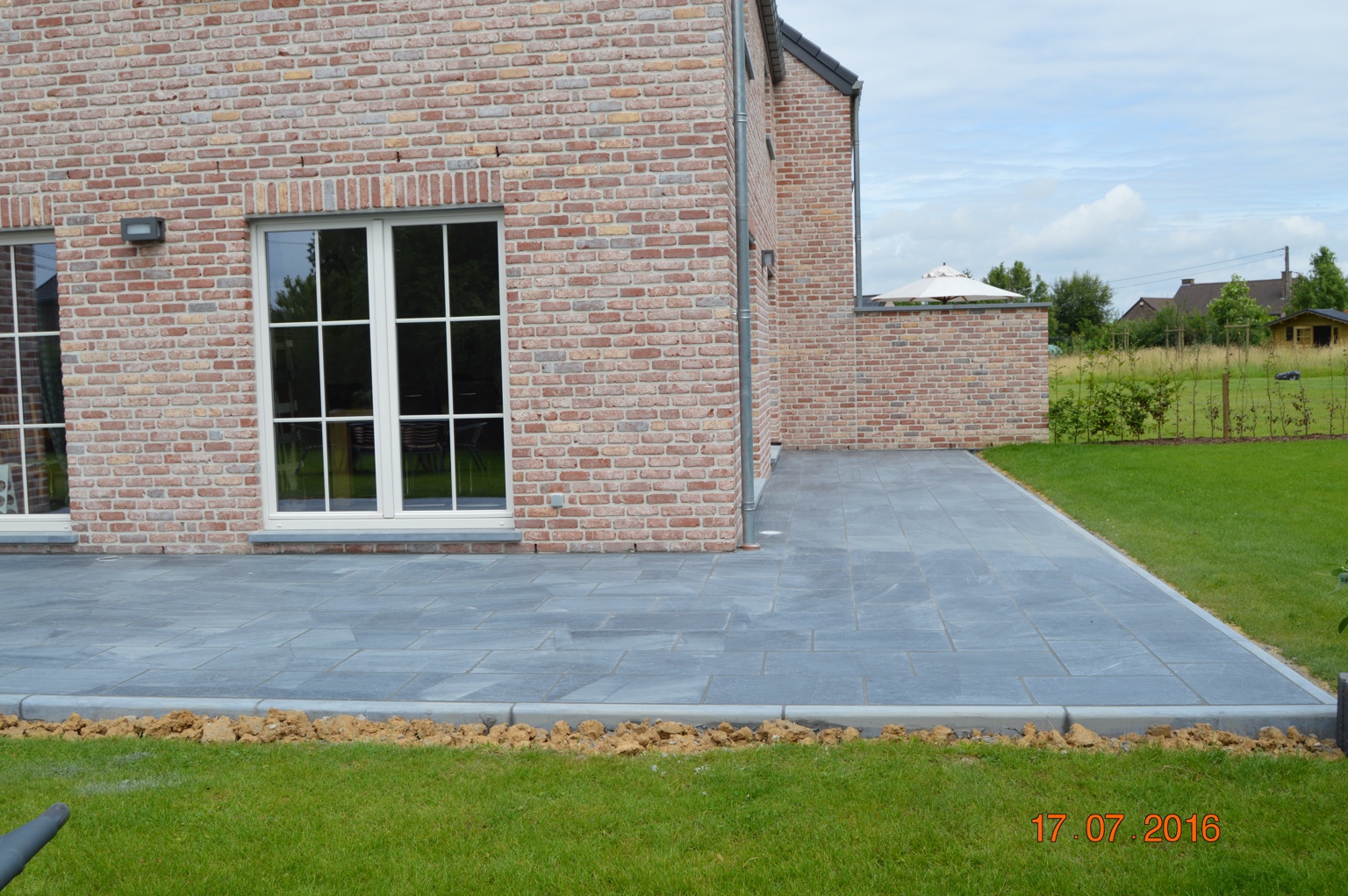 Grande terrasse en pierre naturelle devant une façade en briques